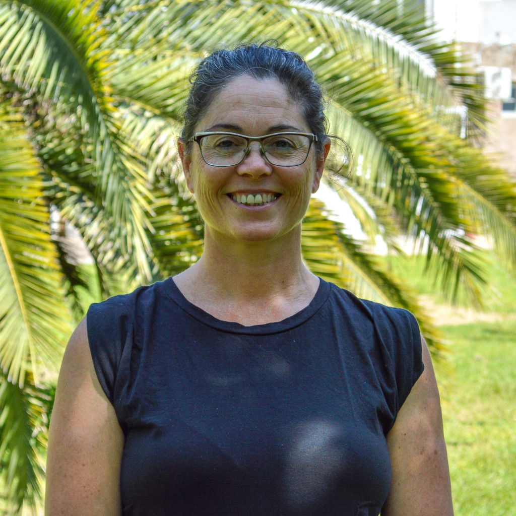 Mg. Analía Cherniz. Mujer sonriendo con lentes. Pelo castaño oscuro. De lentes. Fondo verde de vegetación.