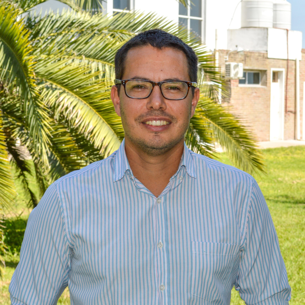 Doctor Mauricio Riveras. Foto de retrato. Hombre sonriendo de lentes. Pelo corto color castaño oscuro. Fondo verde de vegetación.
