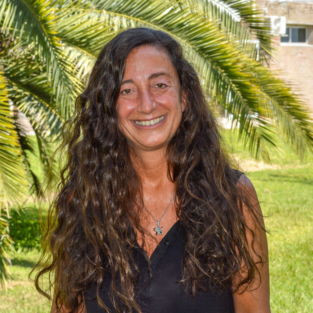 Dra. Paola Catalfamo Formento. Foto de frente, mujer sonriendo pelo largo color castaño. Fondo de vegetación.
